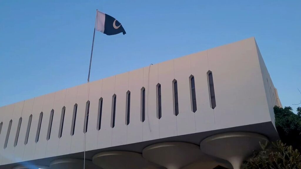 A flag waves proudly atop a building against a clear blue sky, symbolizing national pride and identity